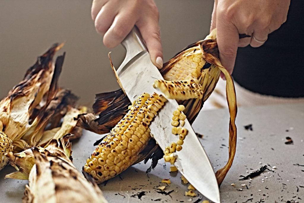 Woman's hand cutting grilled corn from the cob