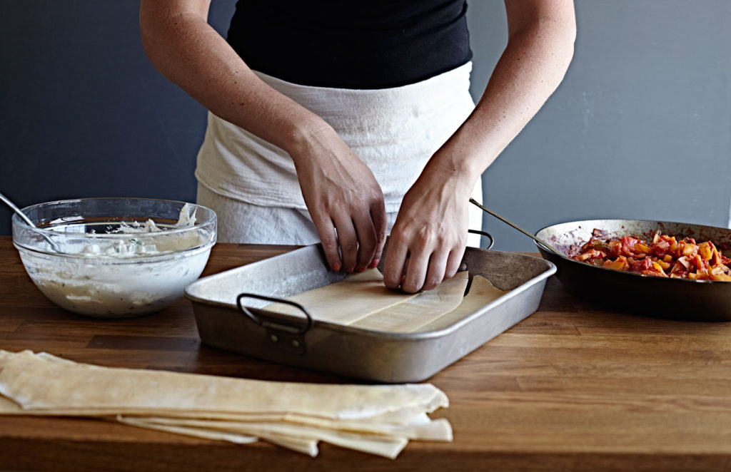 Woman assembling a vegetable lasagna with homemade noodles.
