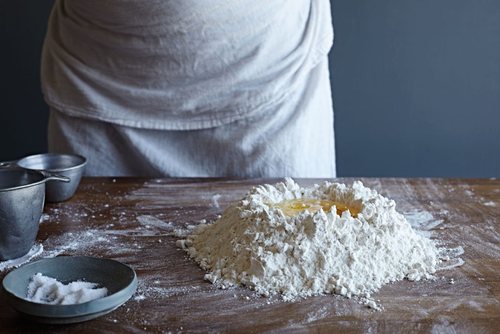 Woman cracking an egg into a pile of flour to make pasta.