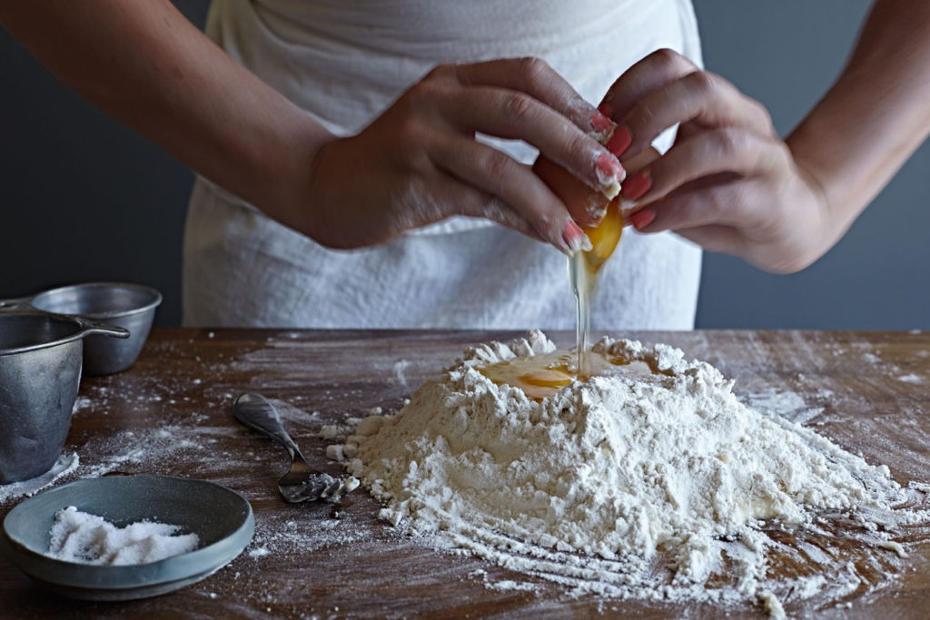 Woman cracking an egg into a pile of flour to make pasta.