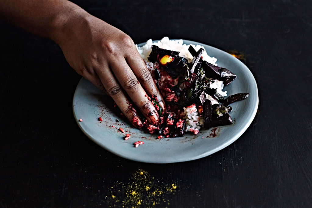 Dark-skinned woman eating Sri Lankan beet curry with her hand.