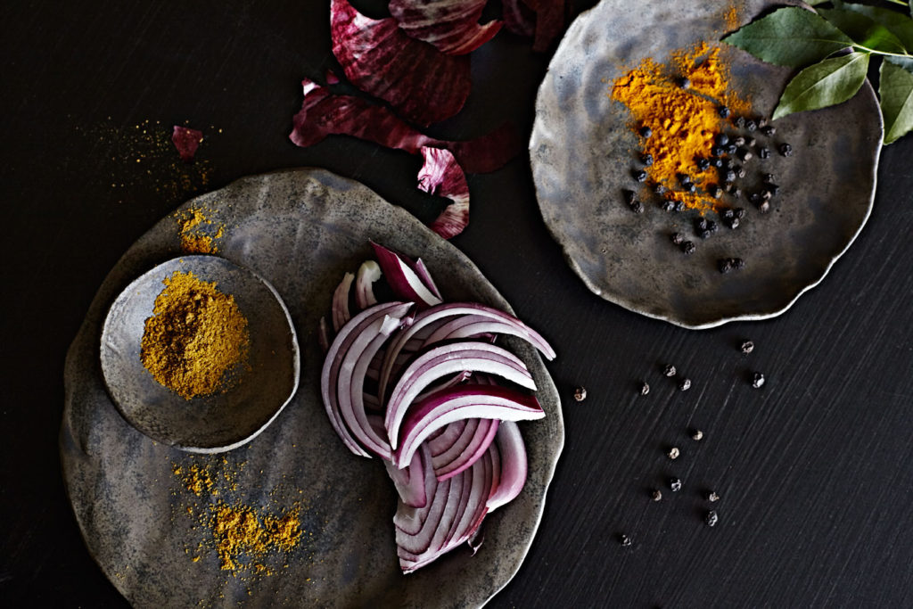 Turmeric, red onion, curry powder and peppercorn ingredient shot on dark handmade dishes.