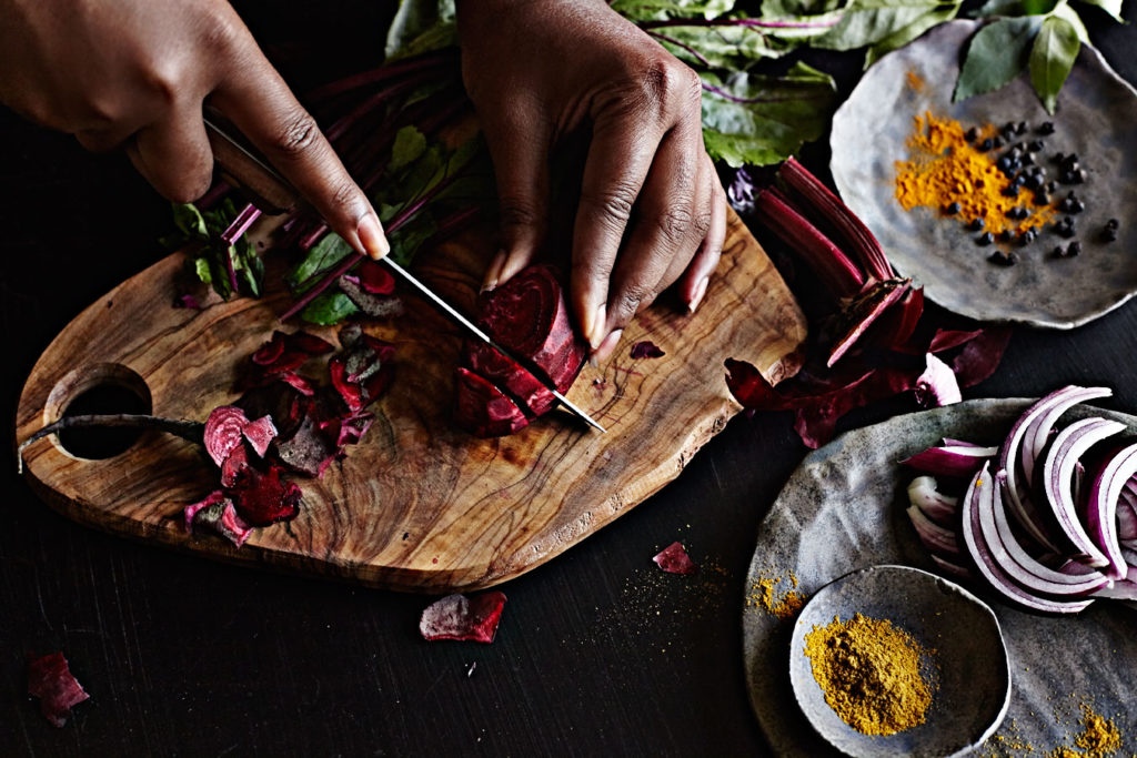 Dark-skinned woman's hands slicing red beets.