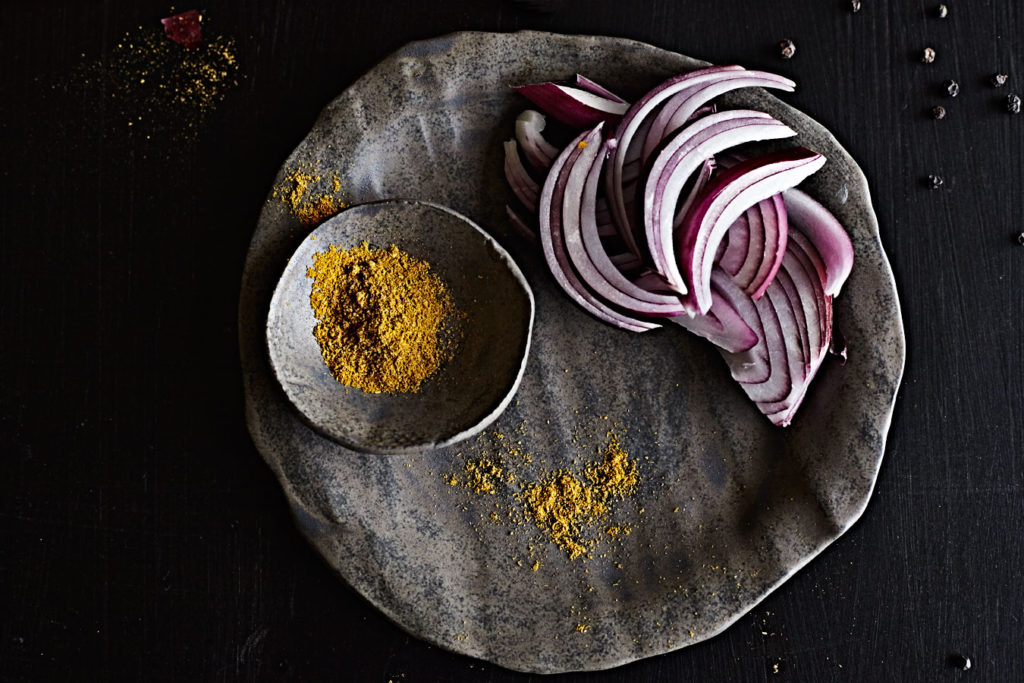 Sliced red onion and curry powder on dark handmade plate.