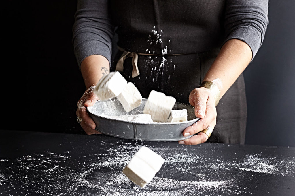 Woman's hand sprinkling powdered sugar over homemade vanilla marshmallows.