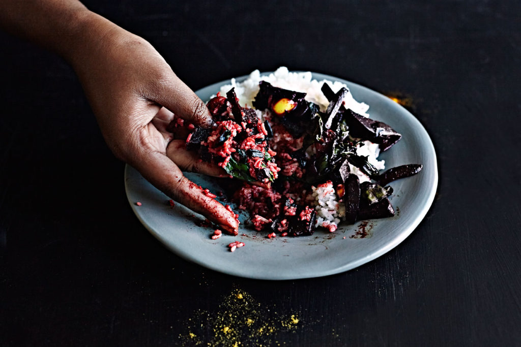 Dark-skinned woman eating Sri Lankan beet curry with her hand.