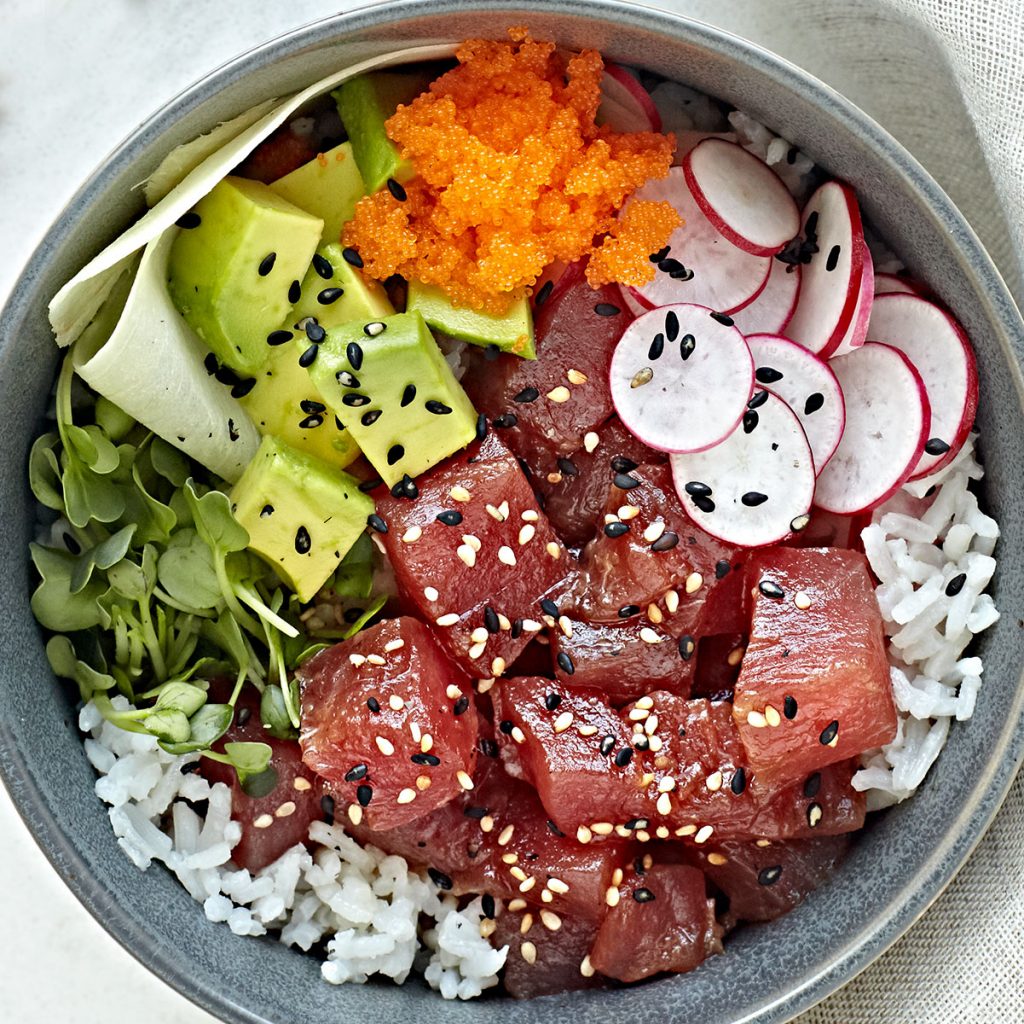 Close up of ahi tuna poke bowl with avocado, radishes, masago, ginger, and sprouts over coconut rice.