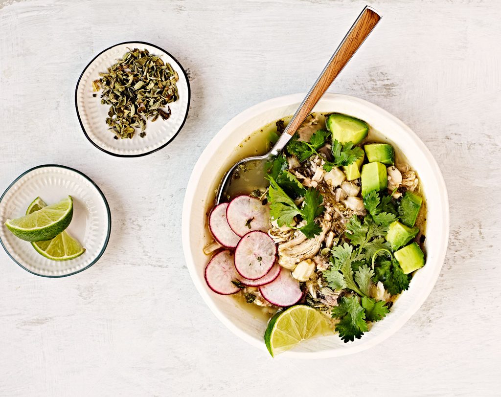 Overhead image of chicken pozole verde soup with lime, avocado, radishes and cilantro.