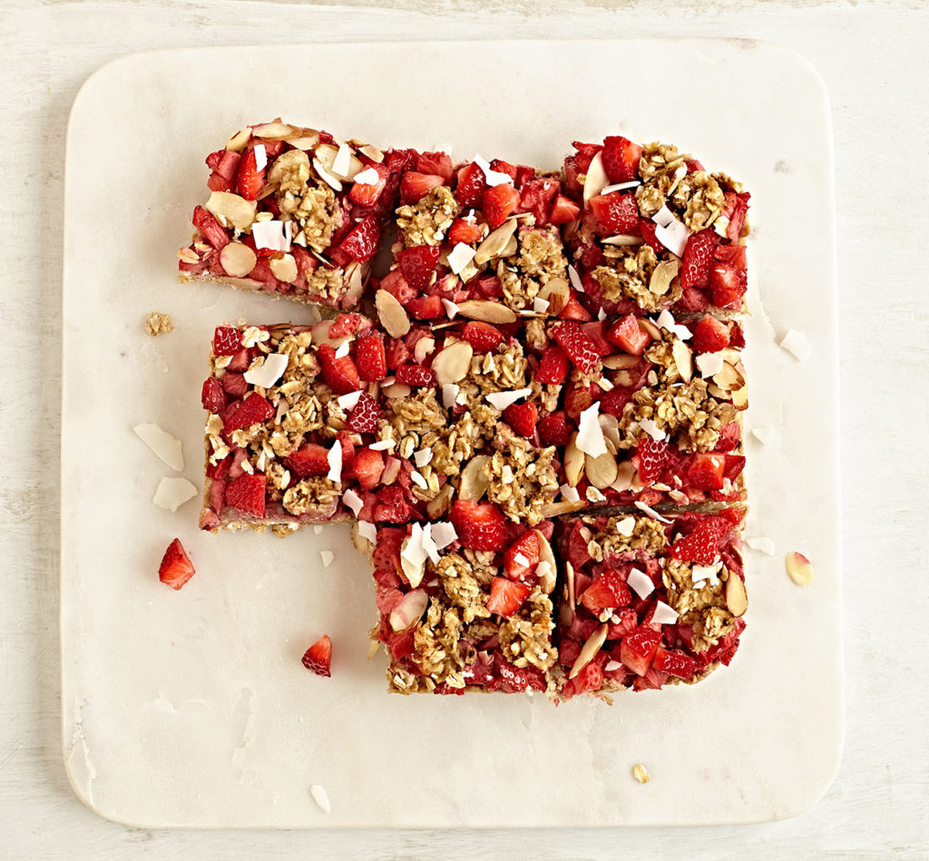 Gluten-free strawberry breakfast bars with almonds, oats, and coconut on marble board.