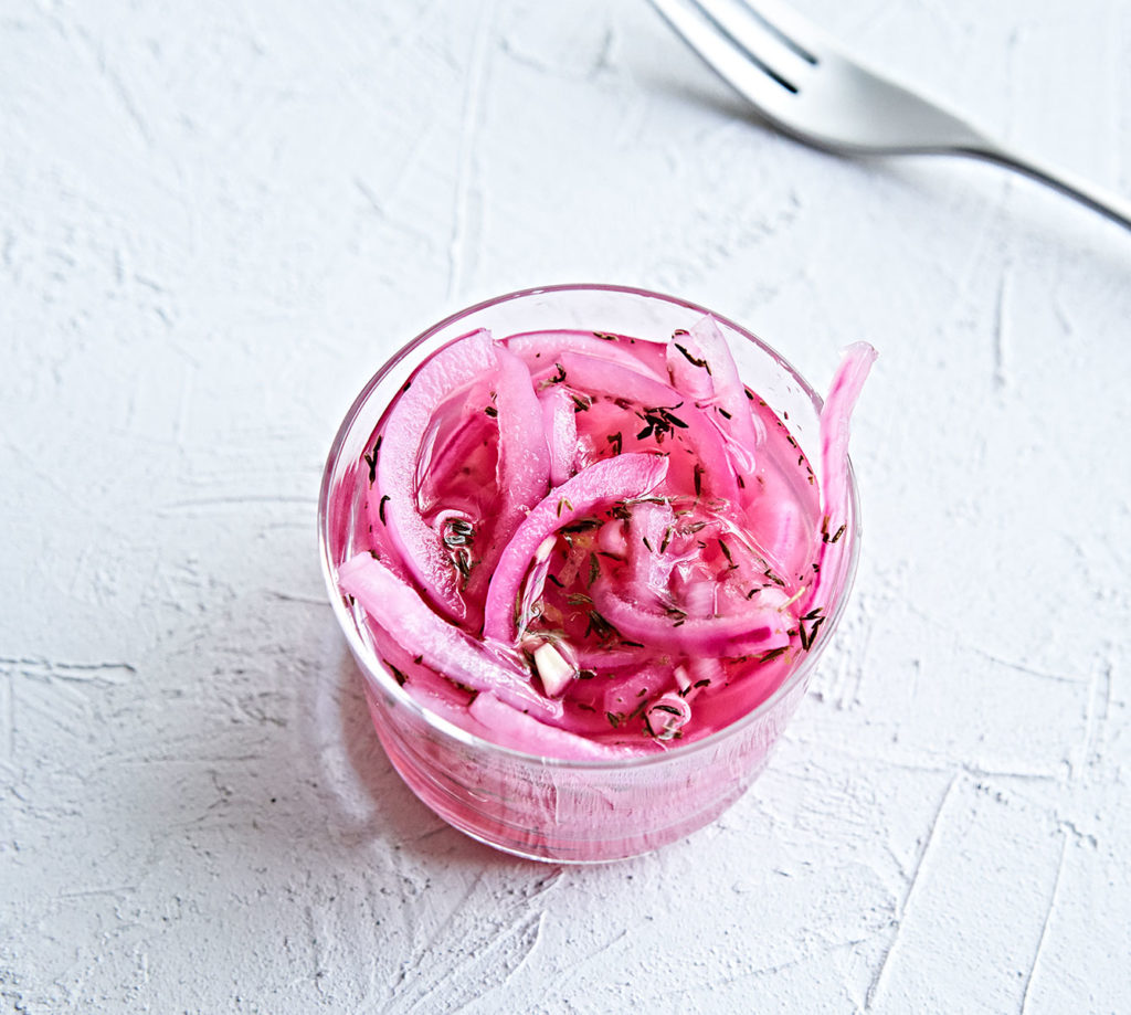 Pickled red onions with herbs in a small glass bowl.