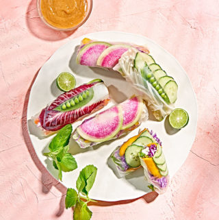 Vegan rainbow spring rolls with watermelon radish, pea pods, and mango on white plate.