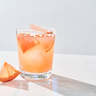 Salty chihuahua grapefruit and tequila margarita with salted rim and grapefruit garnish on marble table.